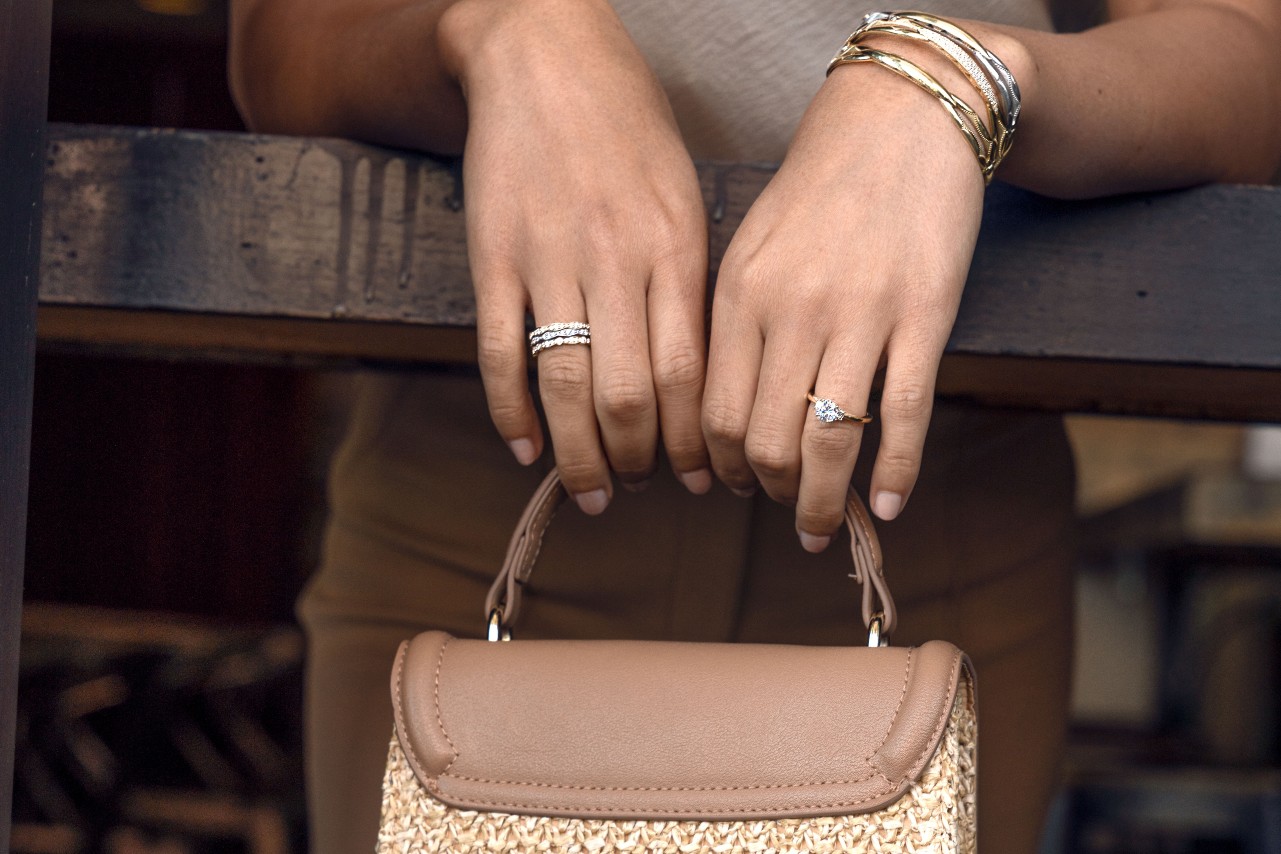 Yellow and white gold diamond bangles by TACORI along with a yellow gold solitaire engagement ring and three diamond fashion rings on the woman’s other hand holding her purse. Yellow and white gold diamond bangles by TACORI along with a yellow gold solitaire engagement ring and three diamond fashion rings on the woman’s other hand holding her purse.