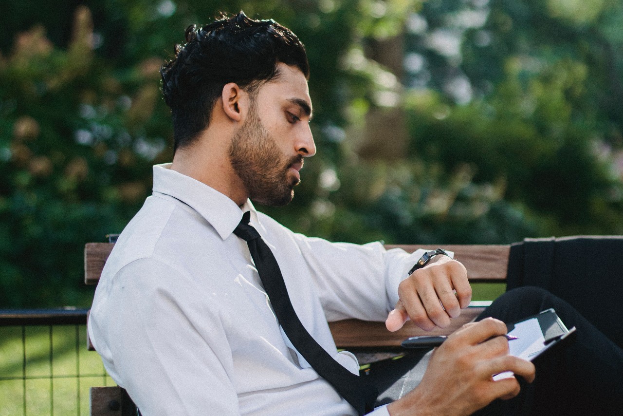 man sitting on a park bench looking at his watch man sitting on a park bench looking at his watch